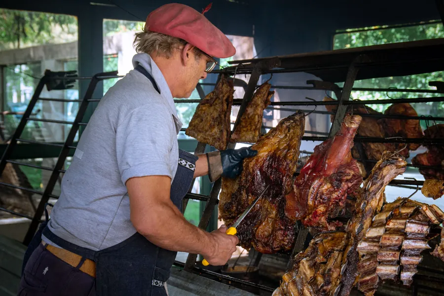Asador cortando cordero y costillares colgados en la parrilla